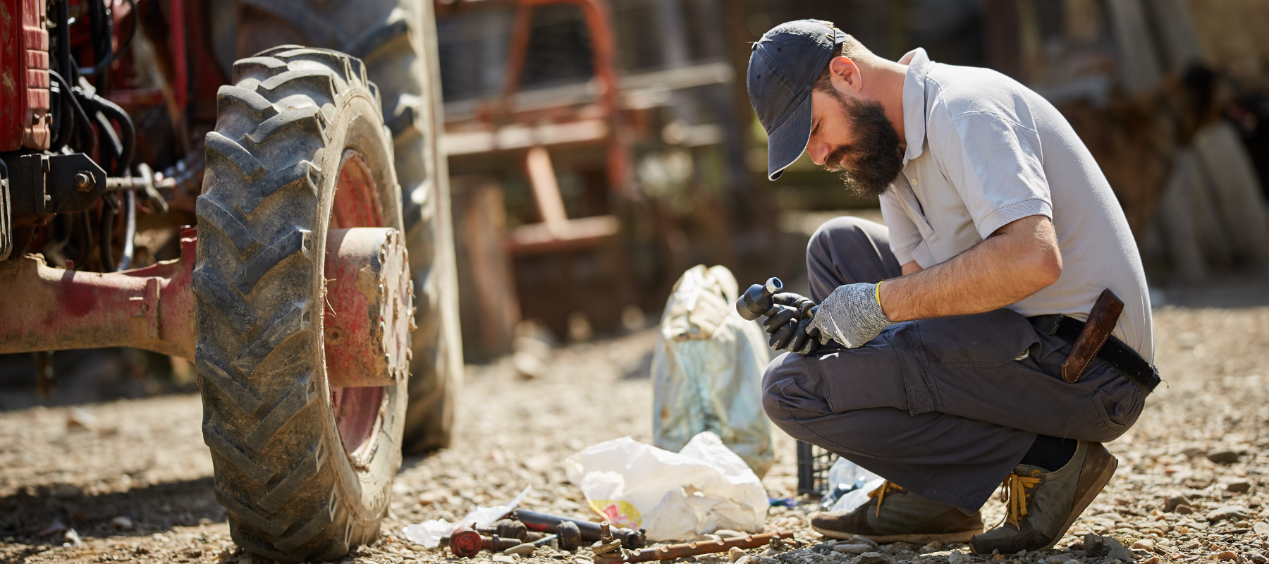 A farmer working on a tractor with hand tools on a clear day.